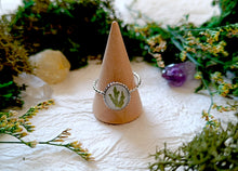 Load image into Gallery viewer, Ring with a nature-themed design on a wooden cone against a natural background with flowers and stones.
